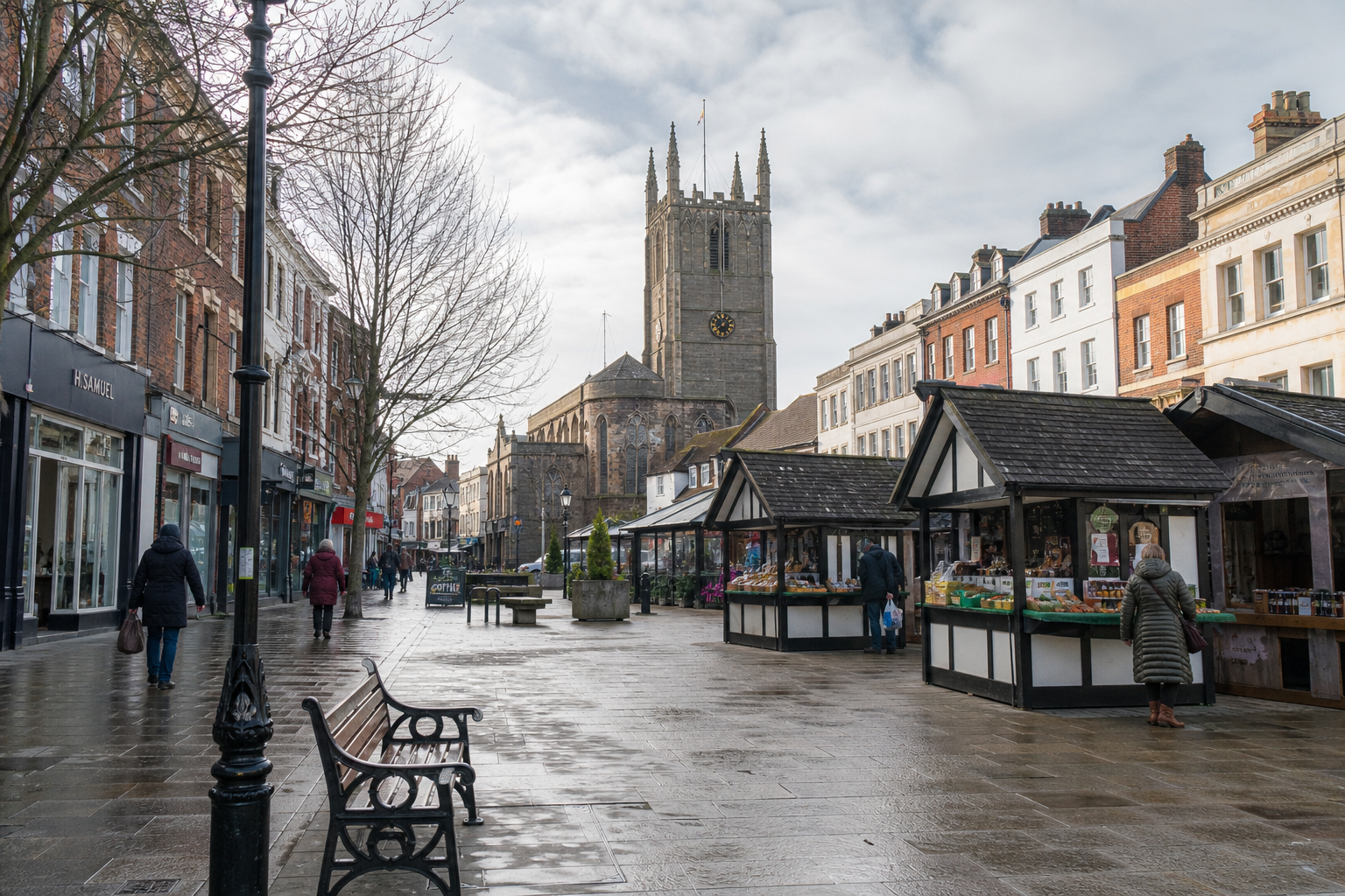 A bustling market street with wooden stalls and a historic church tower in the background on a cloudy day.