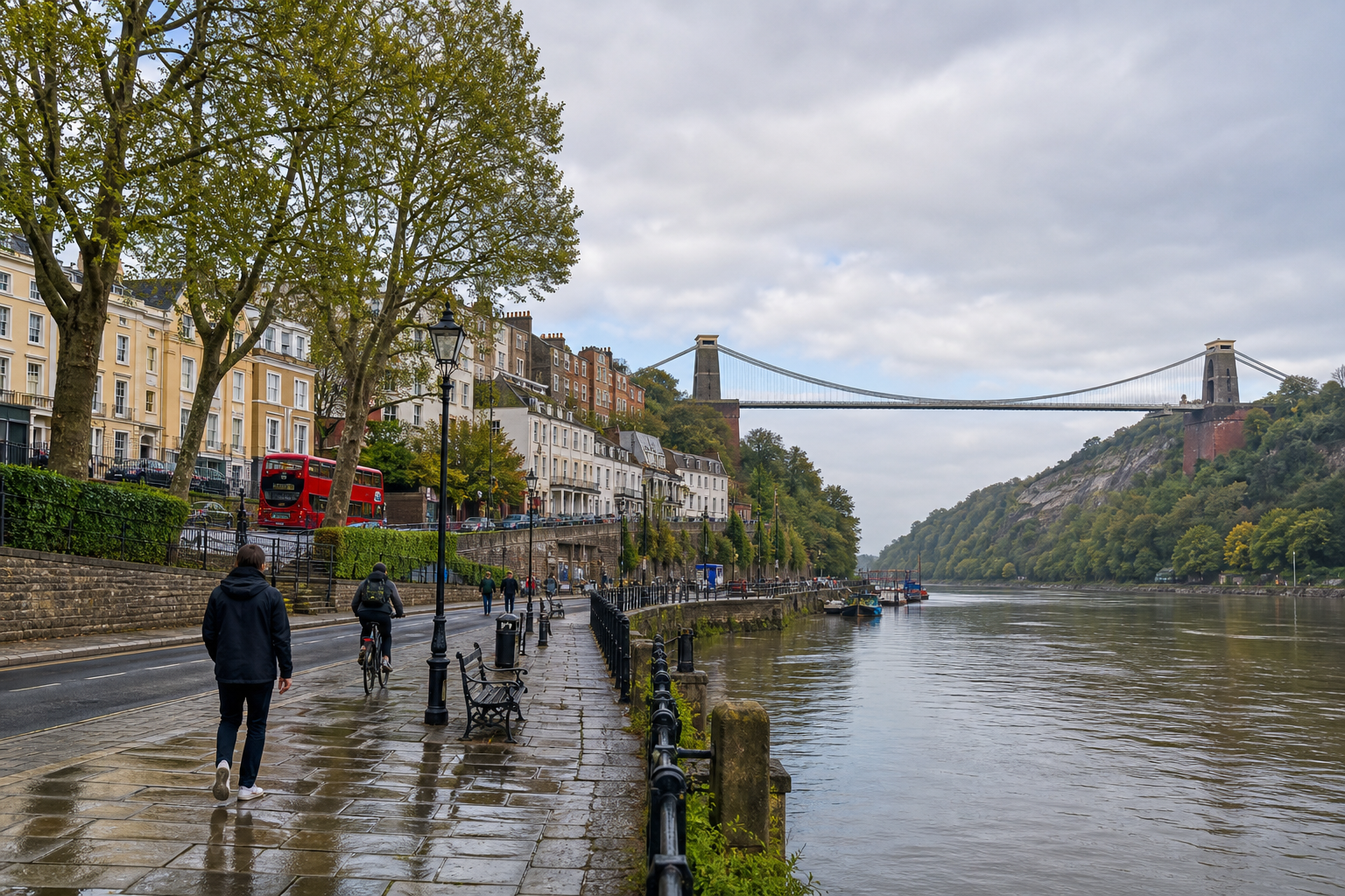 Rainy day by the river with people walking and a bridge in the background.