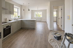 Modern kitchen with grey cabinets and light wooden flooring, featuring painting supplies on a dust sheet in the foreground.
