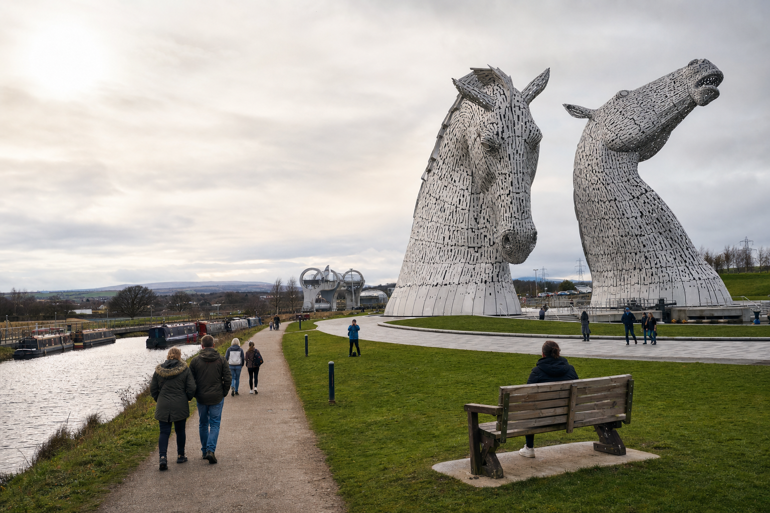 The Kelpies, two large horse head sculptures, stand prominently beside a canal with people walking nearby.