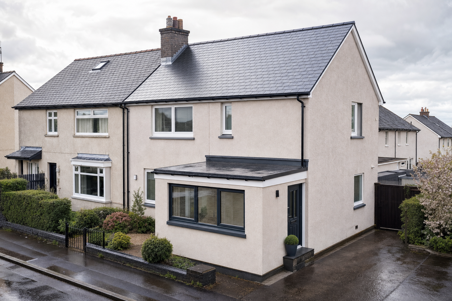 A semi-detached house with a slate roof and modern extension, set on a wet suburban street.