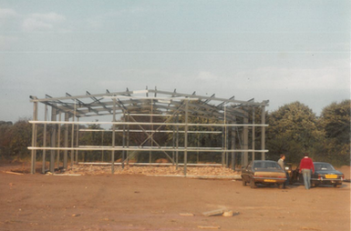 New building steel frame construction, two cars parked nearby.