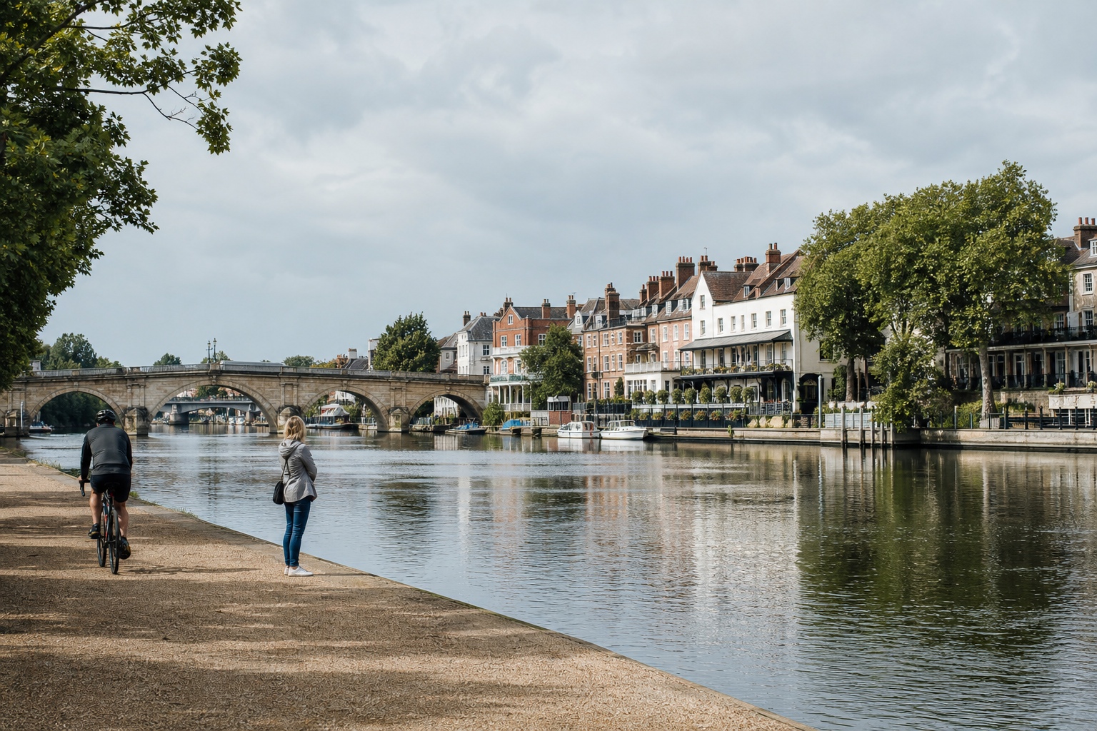 A riverside path with a cyclist and a woman, historic bridge, and Georgian terraced houses in the background.