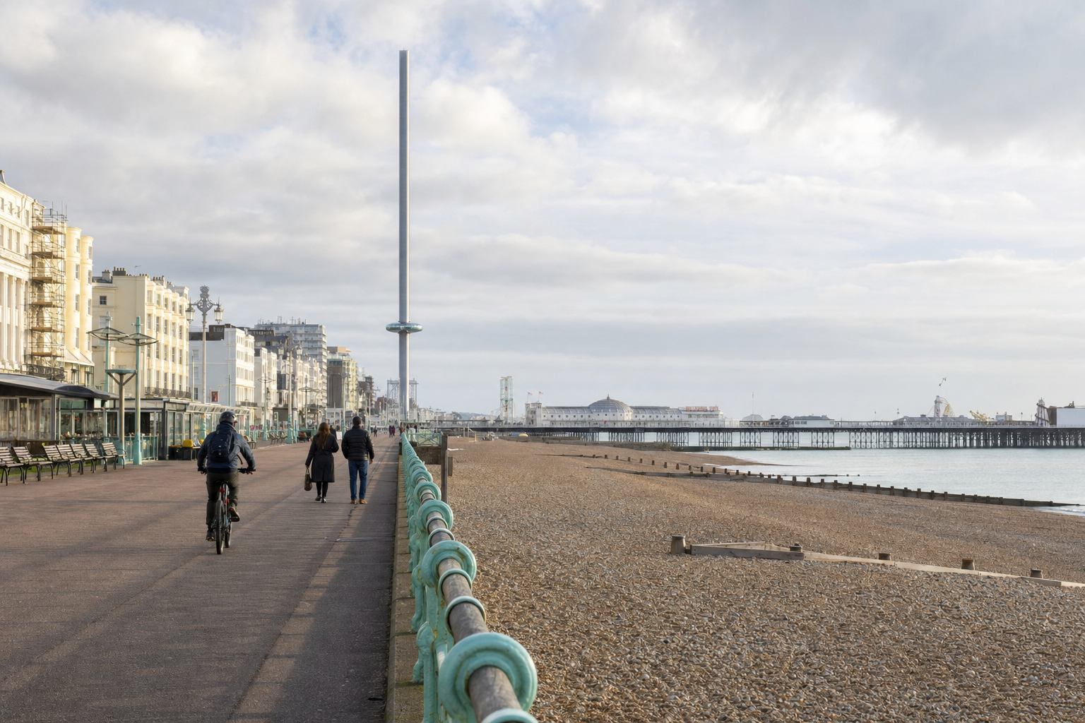 People stroll and cycle along Brighton promenade, with the i360 tower and pier in the background.