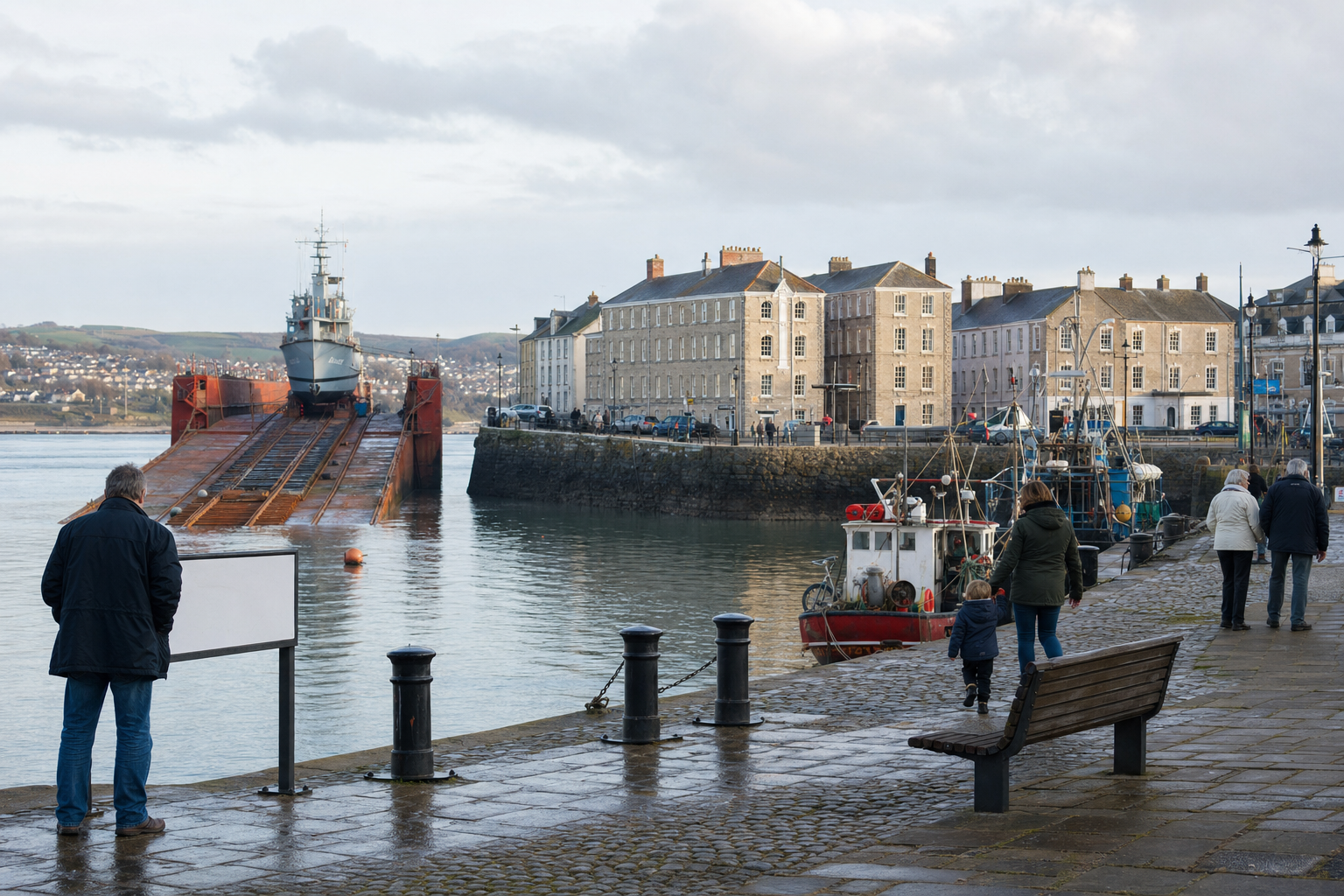 A ship is docked on a ramp beside a charming historic harbour with people walking along the quay.