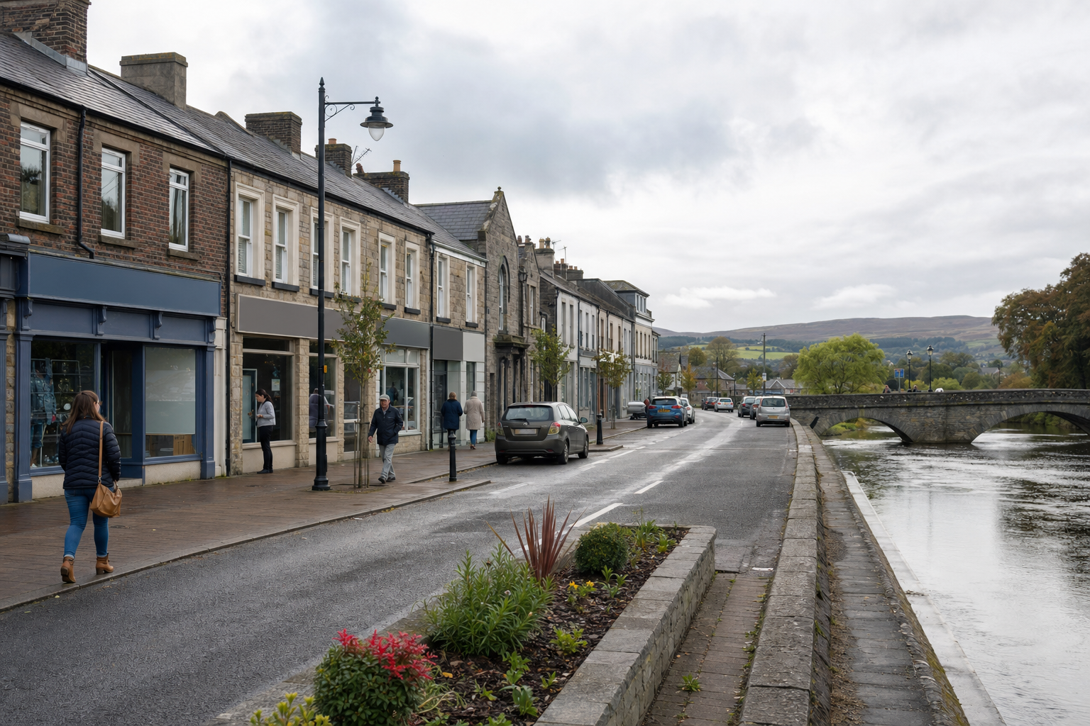 A riverside street with people walking and parked cars, set against a backdrop of hills and an arched stone bridge.
