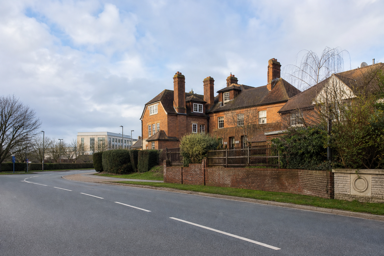 A curved street leads to a large brick house with multiple chimneys under a partly cloudy sky.
