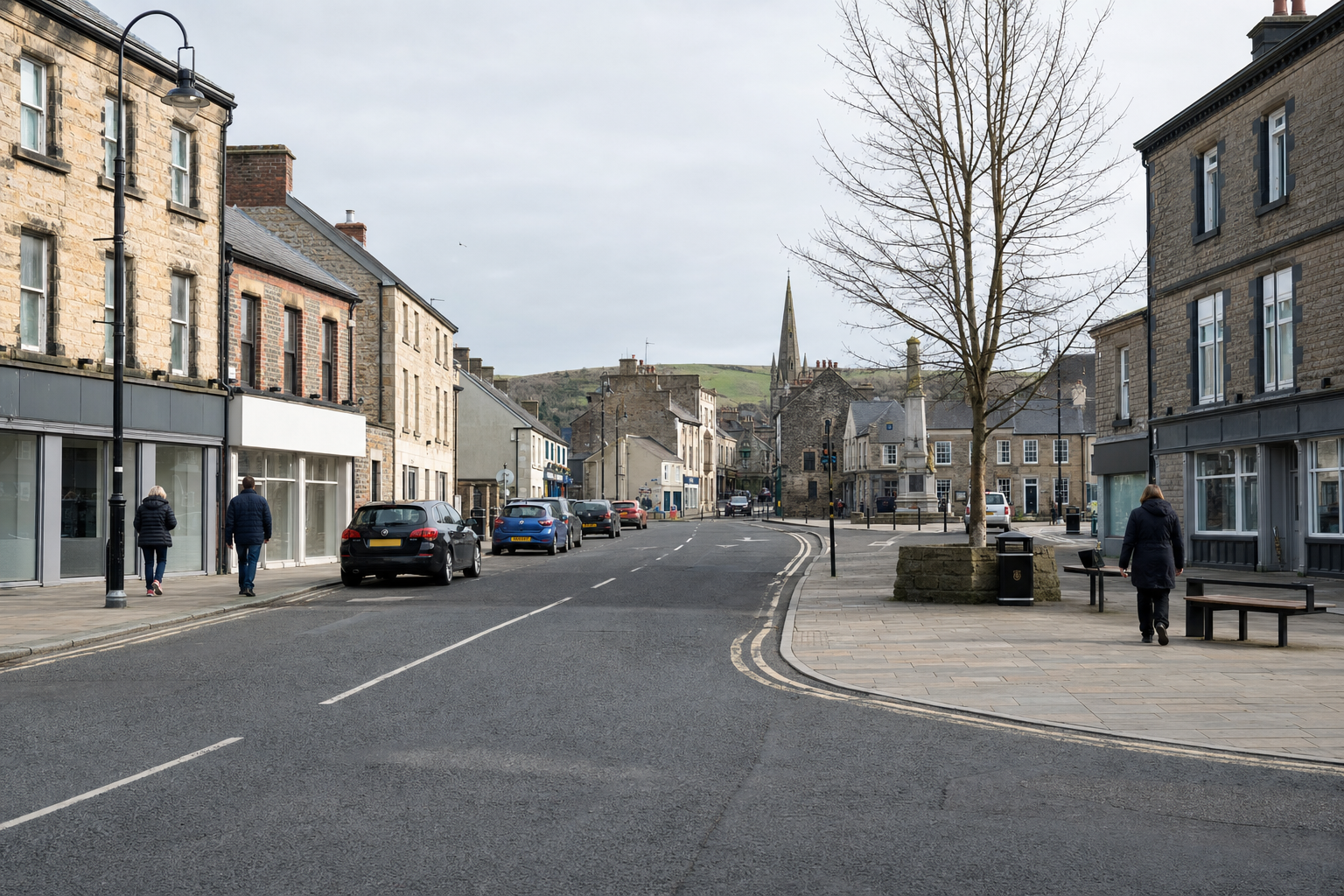 A quiet street in a small town with stone buildings, a few parked cars, and distant hills under a cloudy sky.