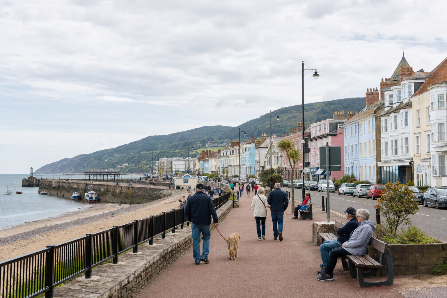 People walking along a seaside promenade with colourful buildings and a view of the beach.