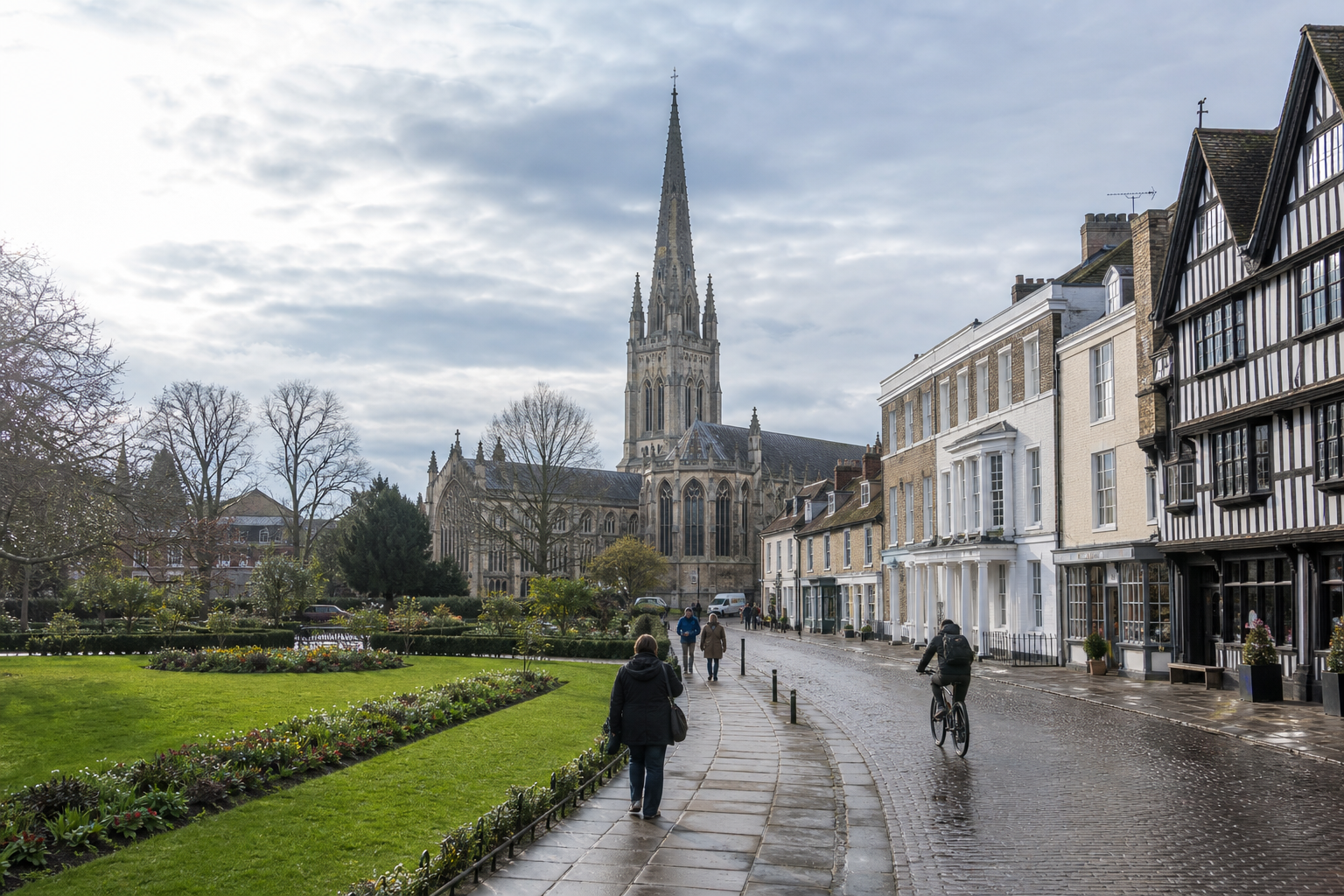 People walking and cycling along a cobblestone street with a historic cathedral and row of buildings in the background.