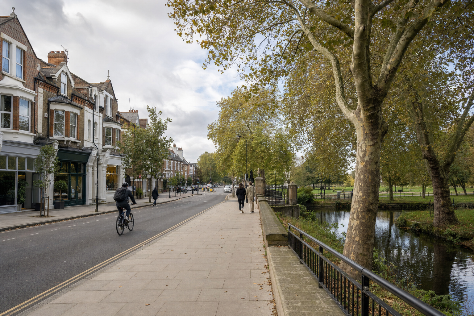 Tree-lined street with cyclists and pedestrians beside Victorian terraced houses and a canal.