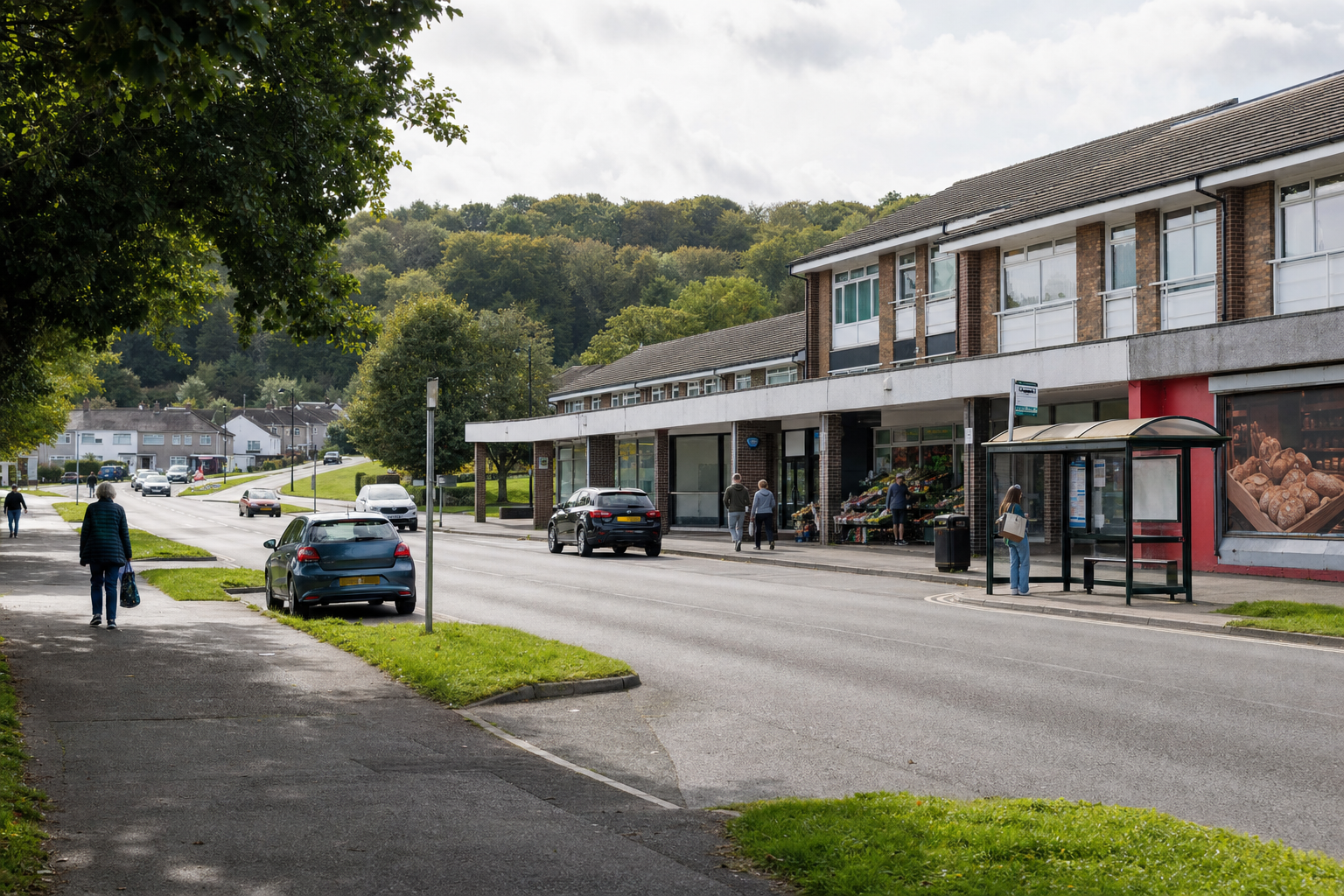 A quiet suburban street scene with parked cars, a bus stop, and a row of shops on an overcast day.