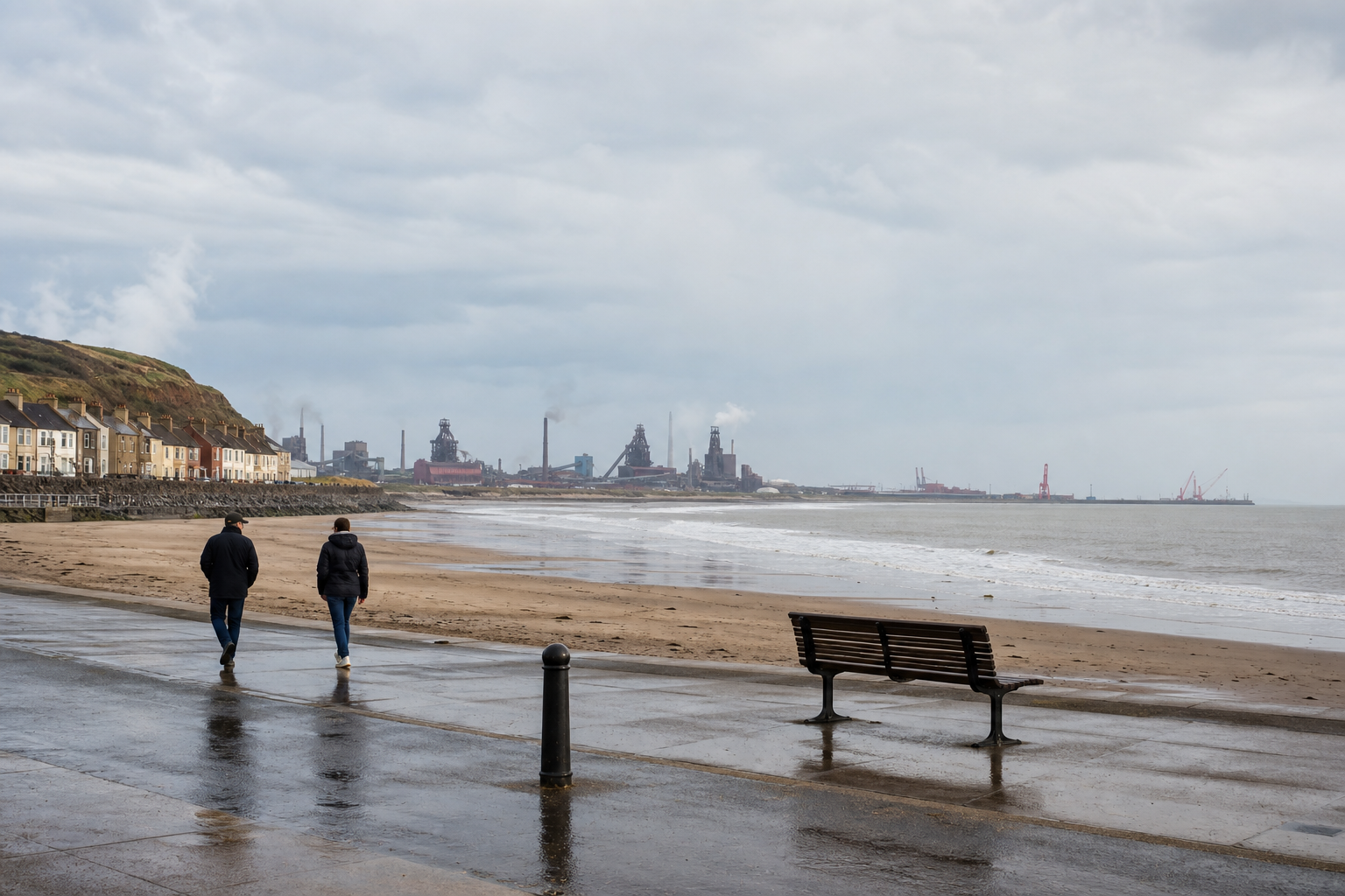 Two people walk along a wet seaside promenade with industrial buildings and smokestacks in the distance.