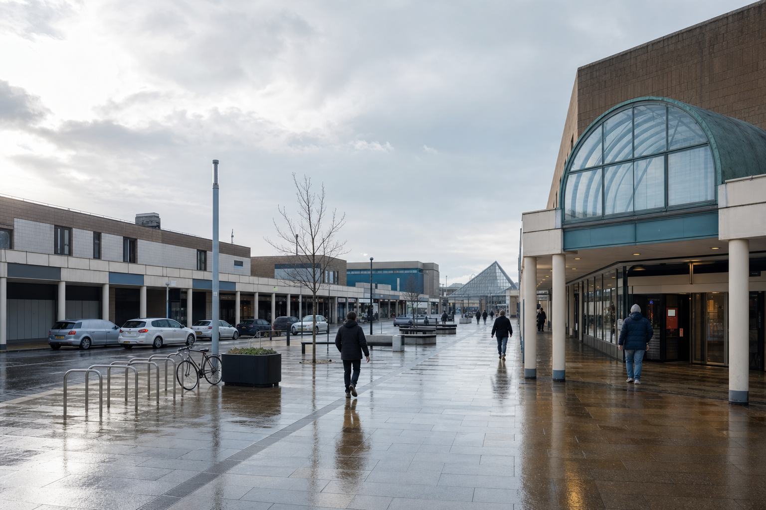 People walking in a wet, modern shopping centre courtyard with a glass pyramid roof in the background.