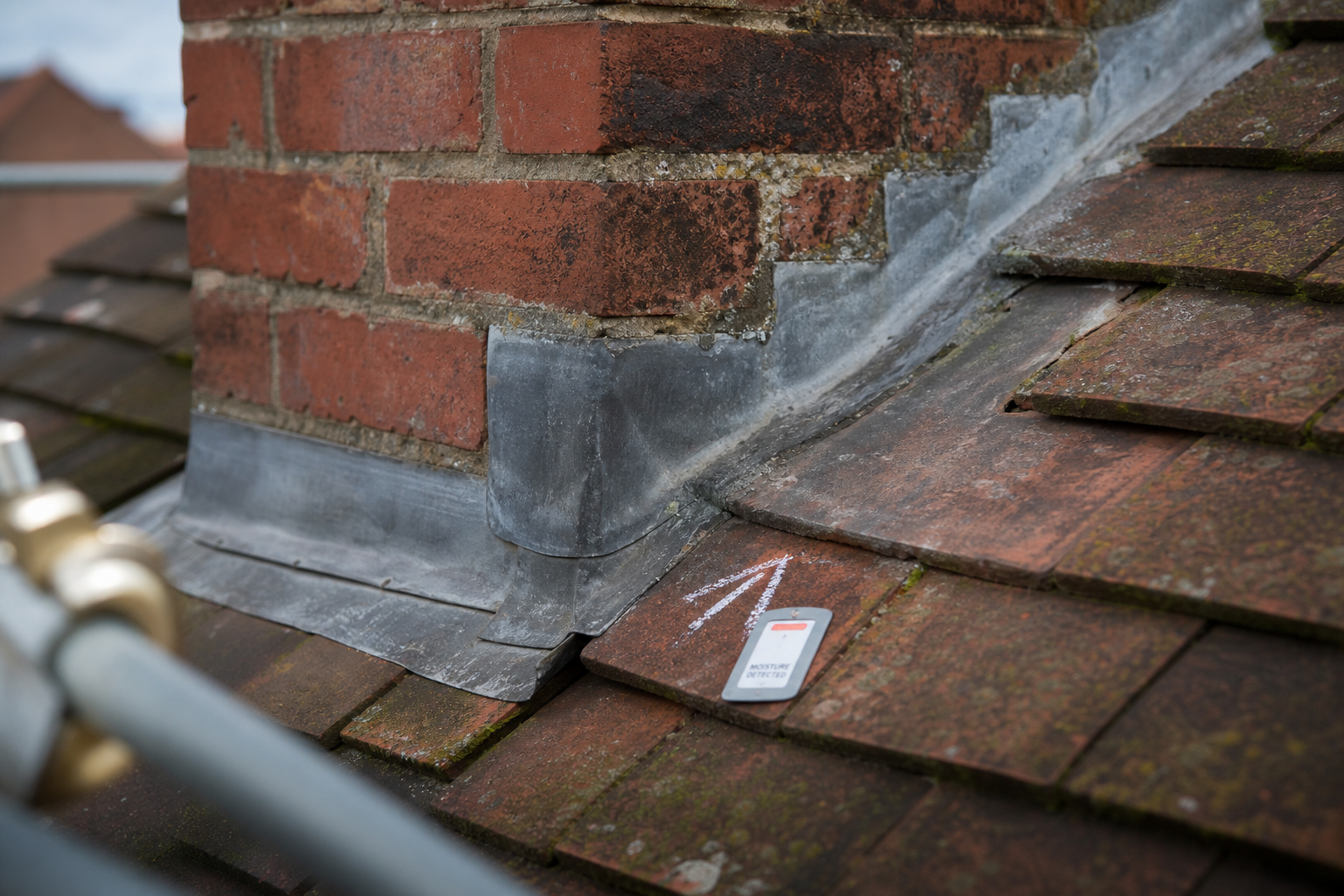 Brick chimney with lead flashing on a tiled roof, marked with chalk indicating moisture detection.