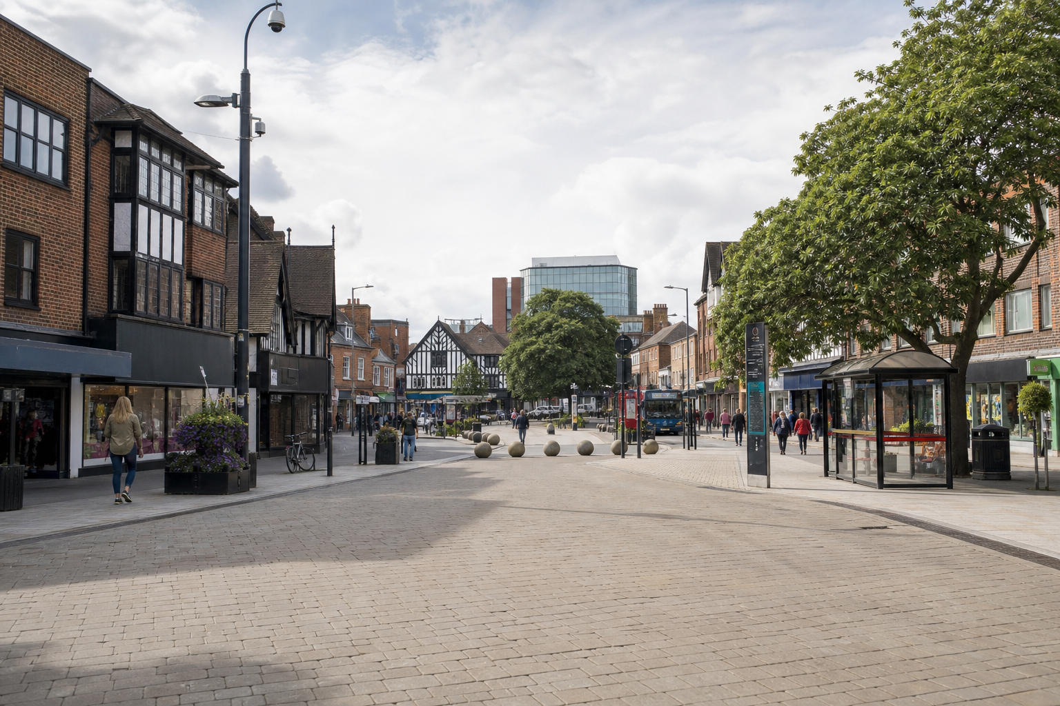 A pedestrianised street lined with traditional and modern buildings, featuring trees and people walking under a partly cloudy sky.