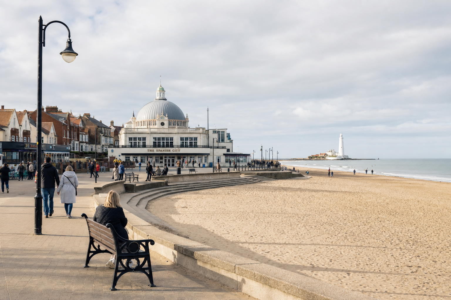 Coastal promenade with Spanish City dome, lighthouse, and people walking near the beach on a cloudy day.