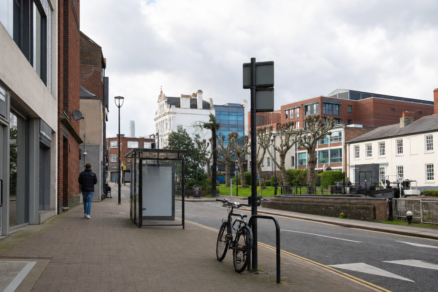 Urban street scene with a bicycle parked near a bus shelter and a person walking along the pavement.