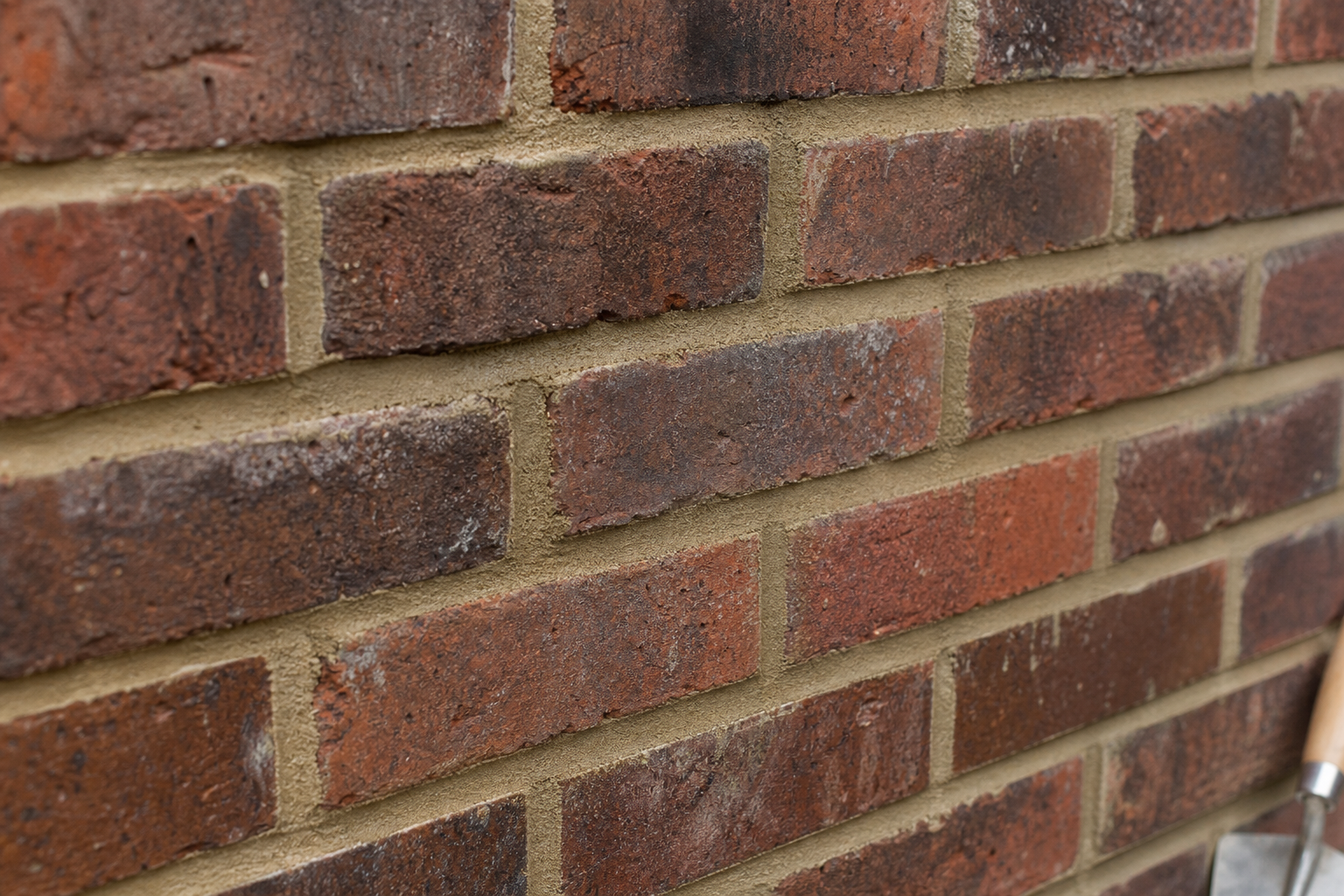 A close-up of a red brick wall with visible mortar joints and a trowel handle on the right edge.