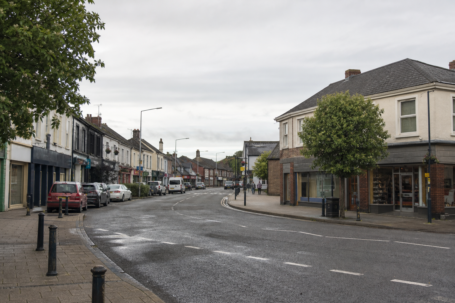 A quiet street with parked cars and terraced shops under an overcast sky.