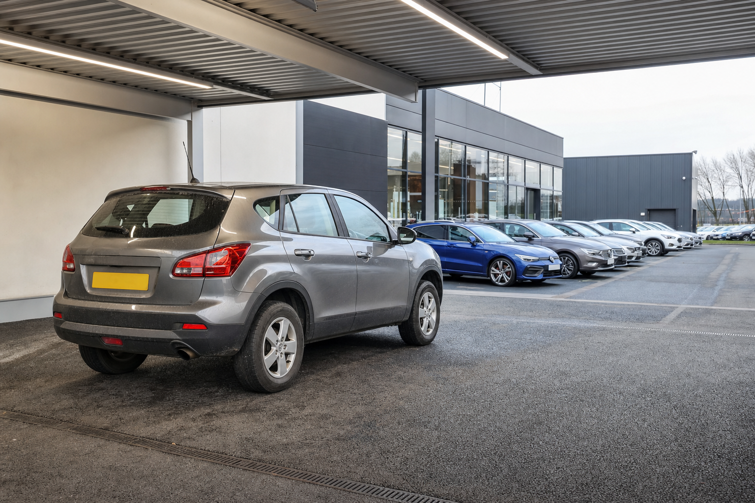 A grey SUV parked at a car dealership with a row of cars in the background.
