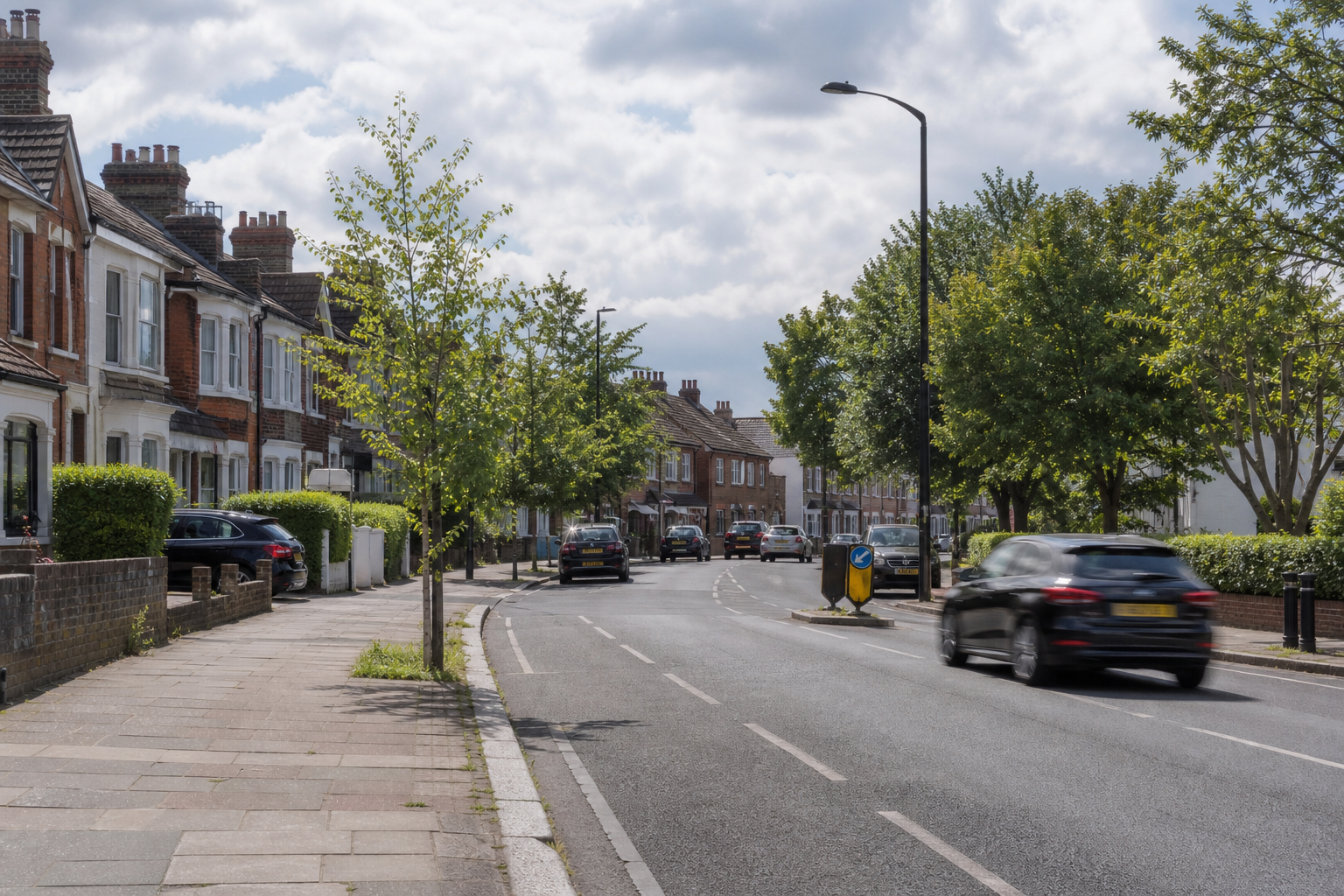 A residential street lined with trees and parked cars under a partly cloudy sky.