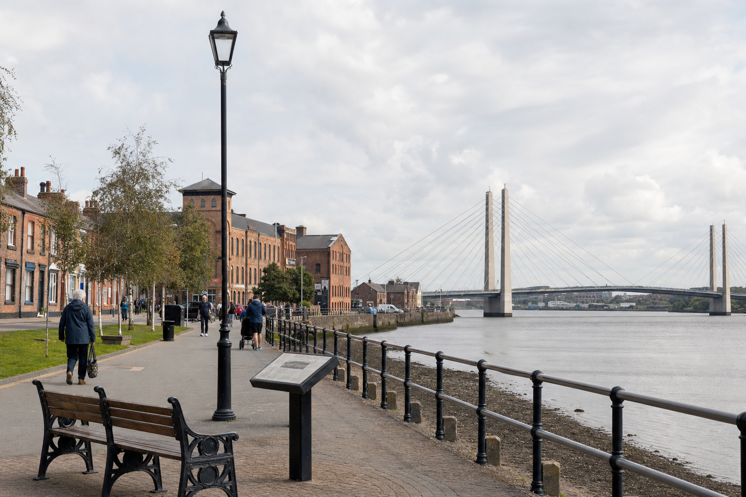 People strolling along a riverside pathway with a modern bridge in the background.