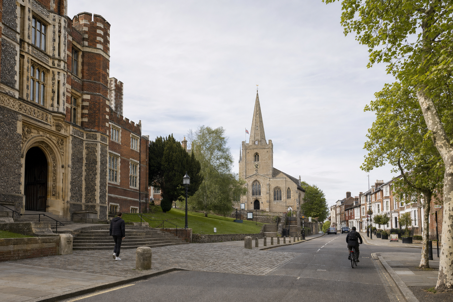 A cyclist and pedestrian on a cobbled street beside a historic church and building lined with trees.