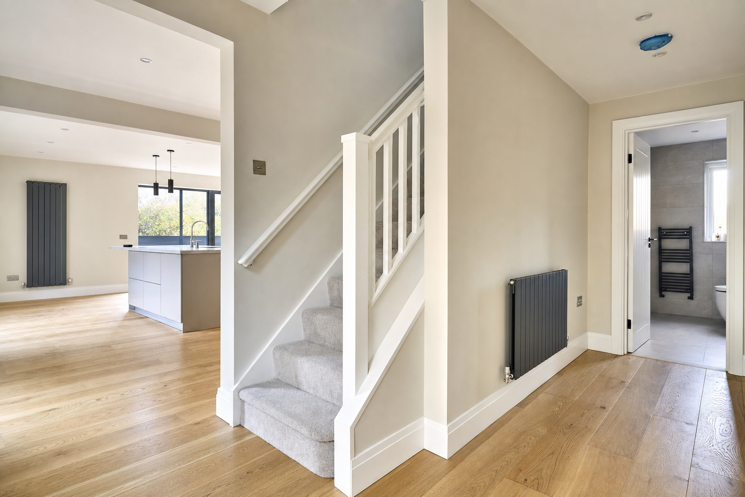 Modern interior with a wooden-floored hallway, grey staircase, and view into a kitchen and bathroom.