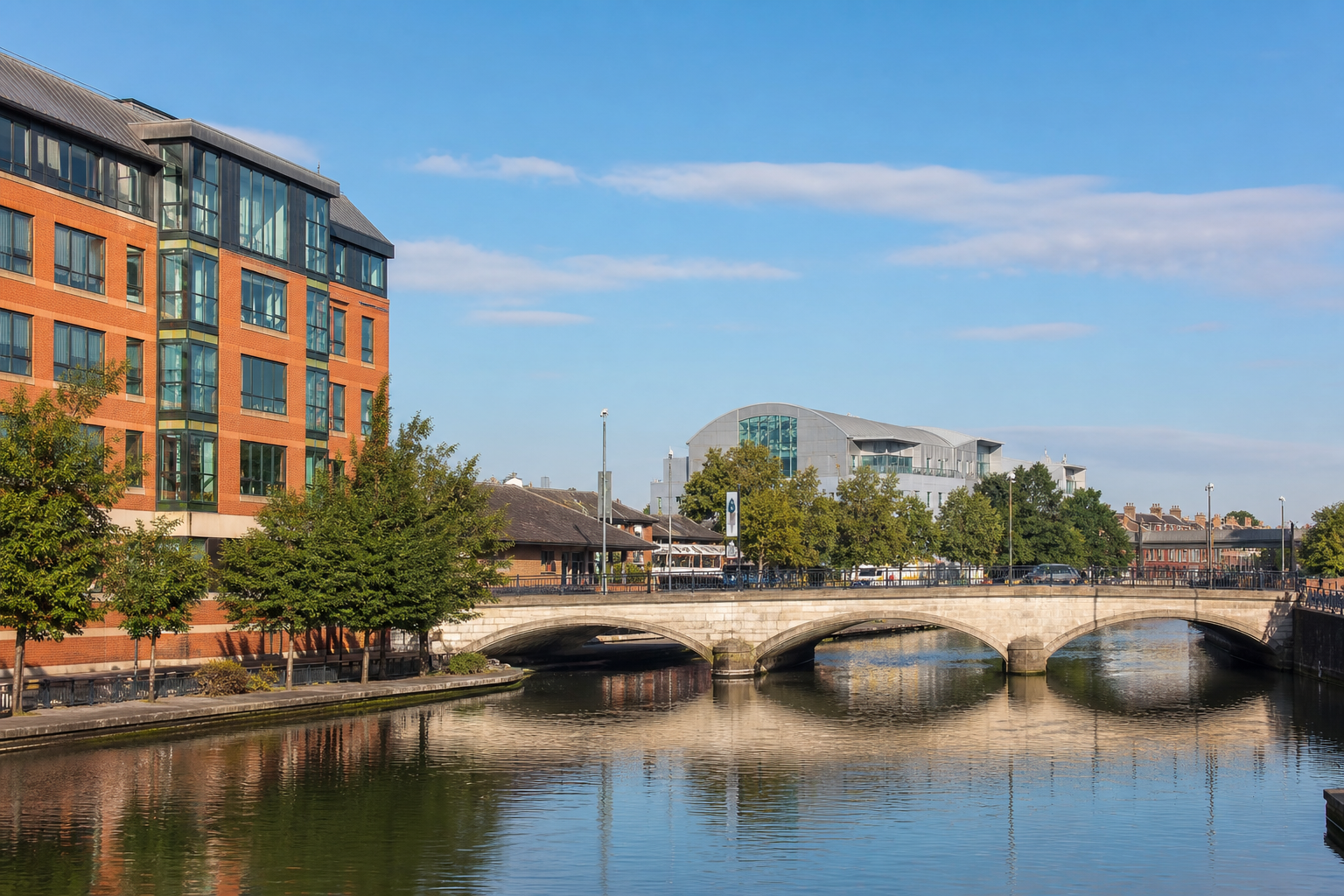 A riverside view with modern buildings and a stone bridge under a clear blue sky.