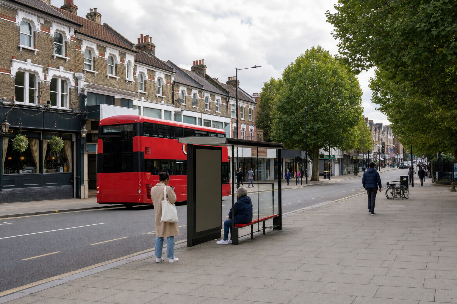 A red double-decker bus passes a bus stop on a tree-lined street with Victorian terraced buildings.
