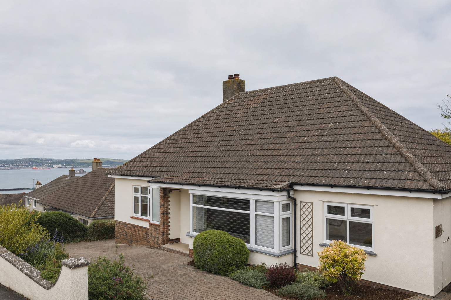 A bungalow with a large bay window and landscaped front garden overlooks a coastal view.