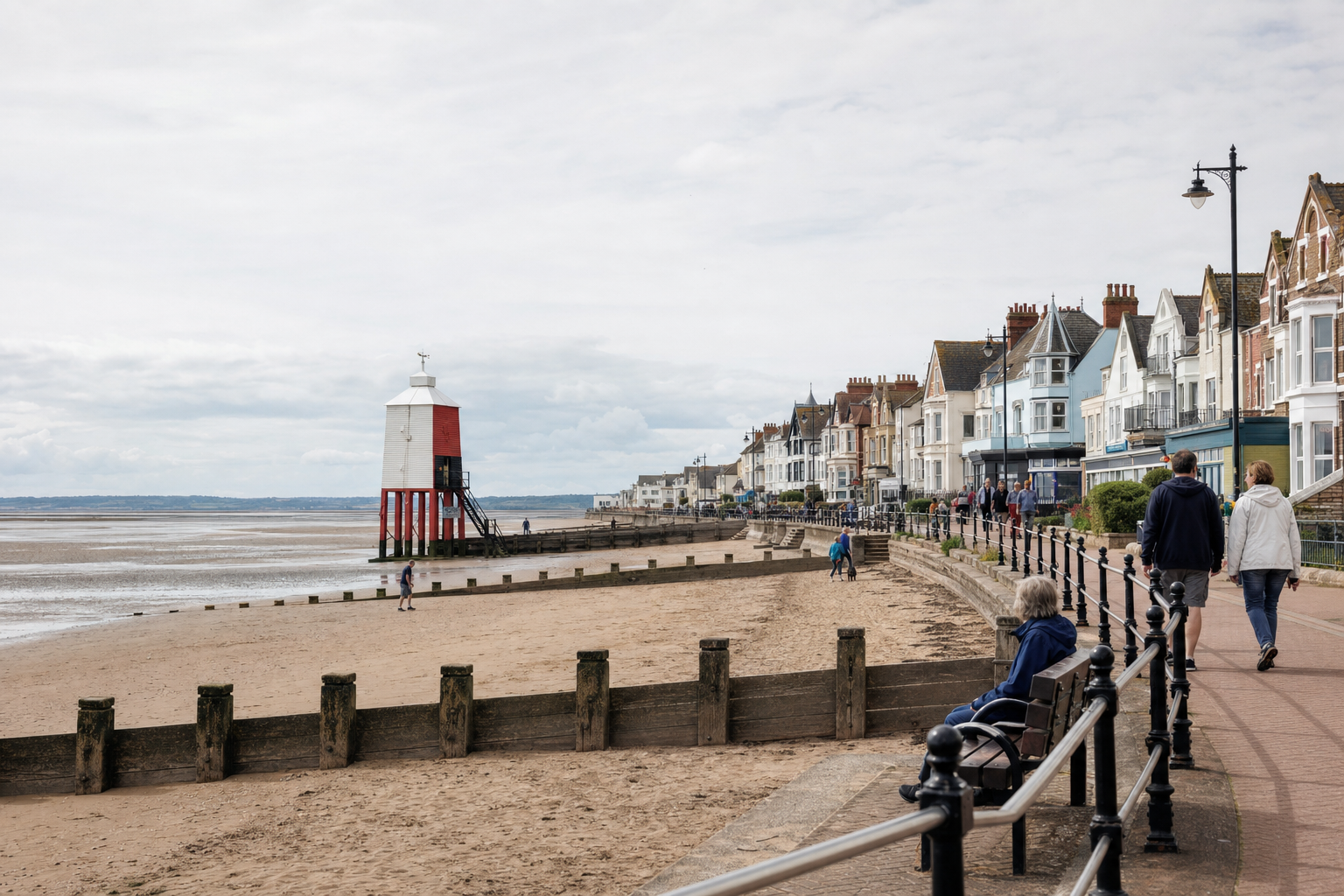 A sandy beach with a distinctive red and white lighthouse and a row of traditional seaside houses in the background.
