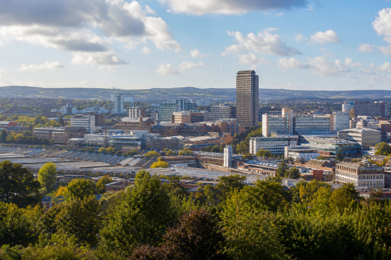 Urban skyline view with tall buildings, greenery, and a blue sky with scattered clouds.