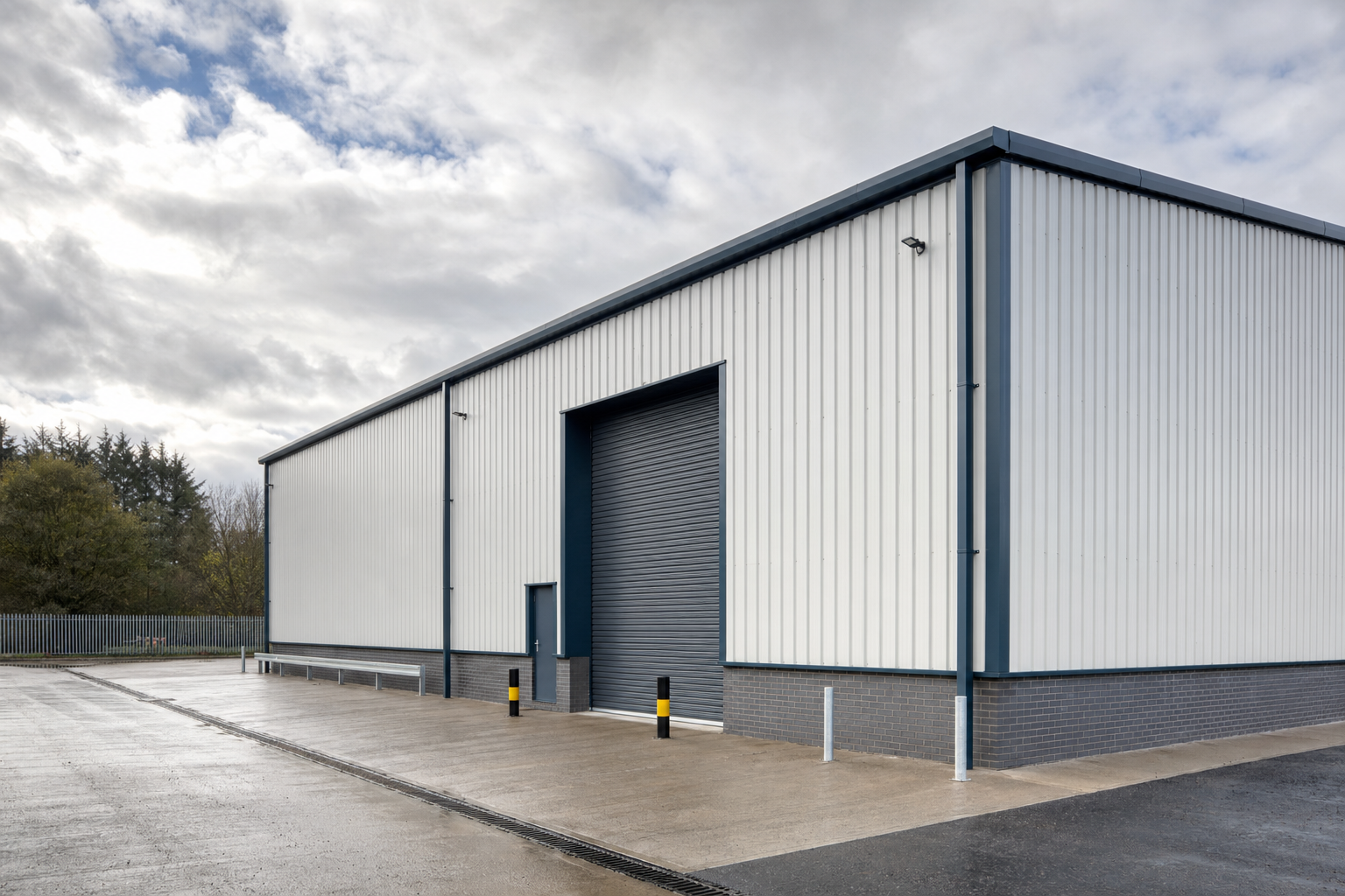 Modern industrial warehouse with a large grey roller door under a cloudy sky.