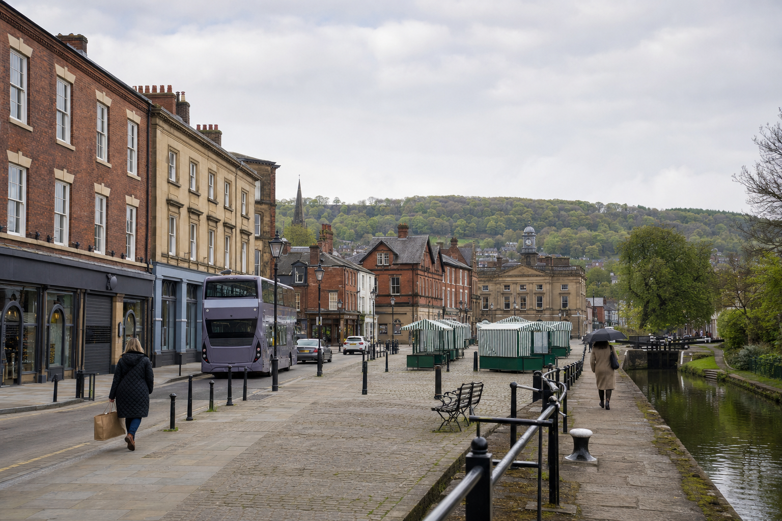 A quiet street by a canal on a cloudy day, featuring a double-decker bus, market stalls, and historic buildings.