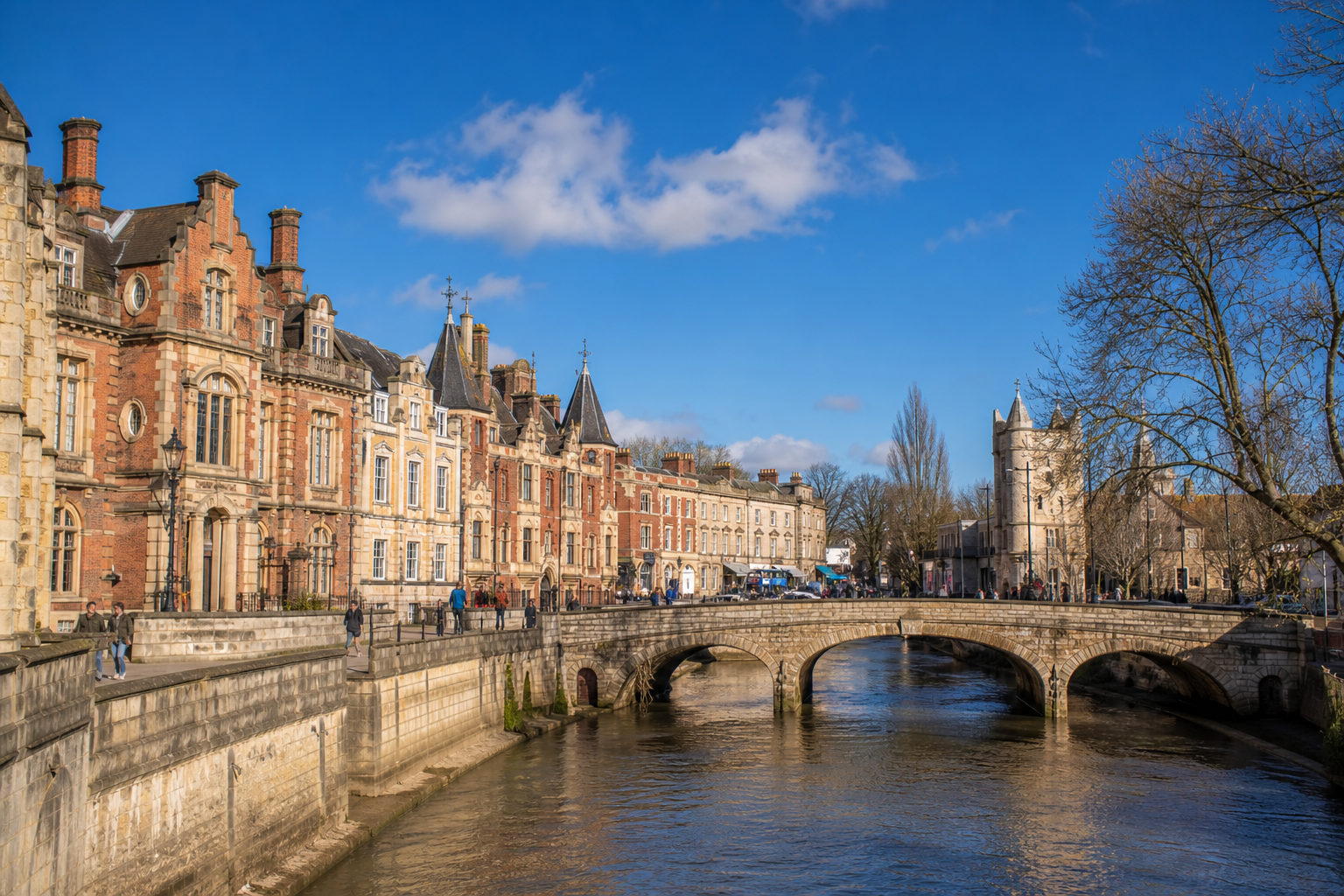 Historic buildings and a stone bridge over a river under a clear blue sky.