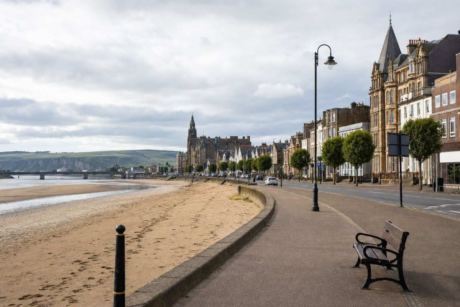 A scenic seaside promenade lined with historic buildings and a sandy beach under a cloudy sky.