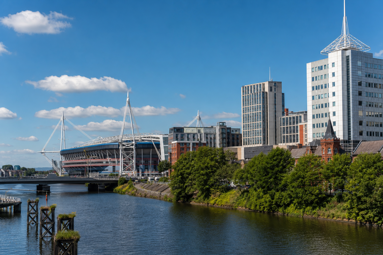 Cityscape with modern buildings and a stadium by a river under a clear blue sky.