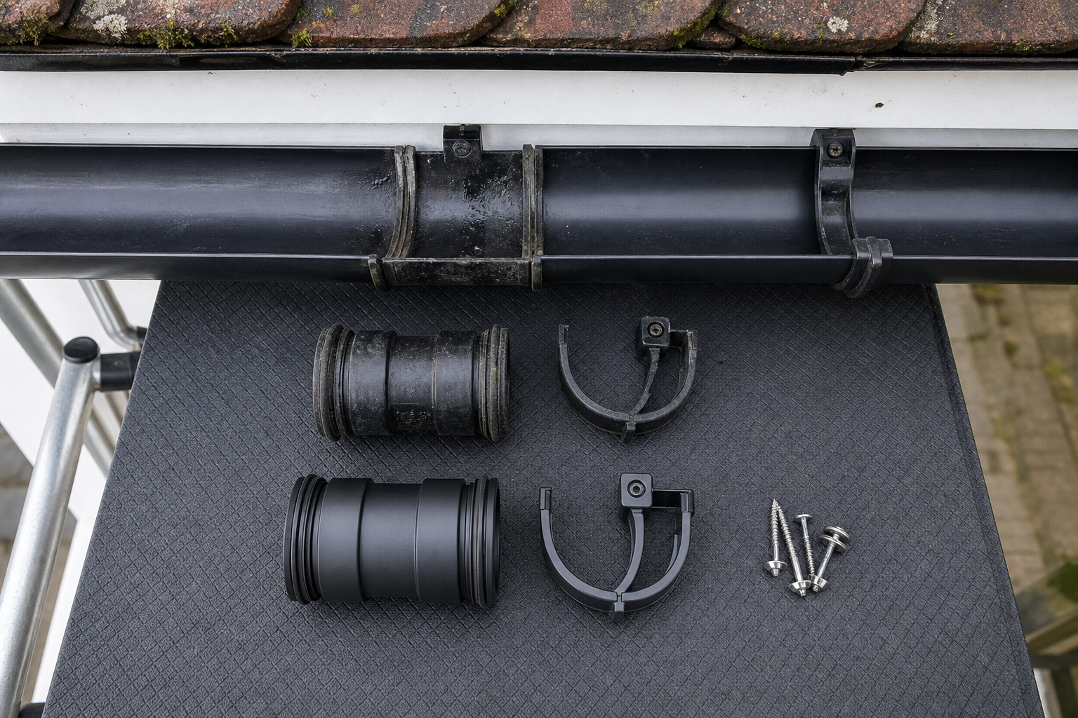Roof gutter with two sets of plastic connectors, support brackets, and screws on a textured surface.