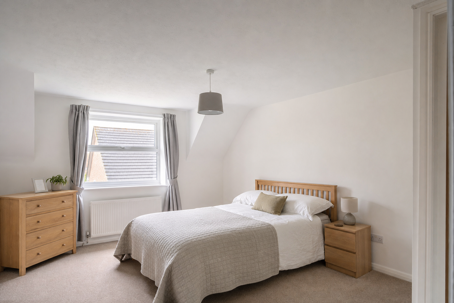 Minimalist bedroom with a wooden bed, neutral bedding, a bedside table, and a chest of drawers by a window.