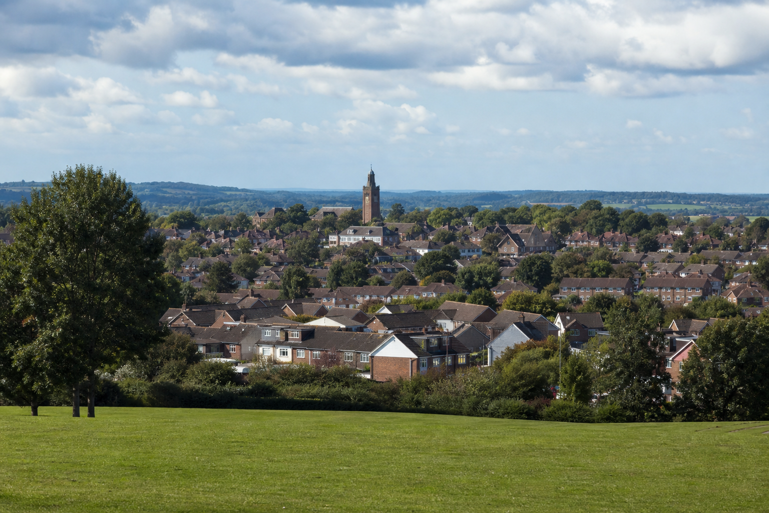 A scenic view of a town with a prominent church tower set against a backdrop of rolling hills and cloudy skies.