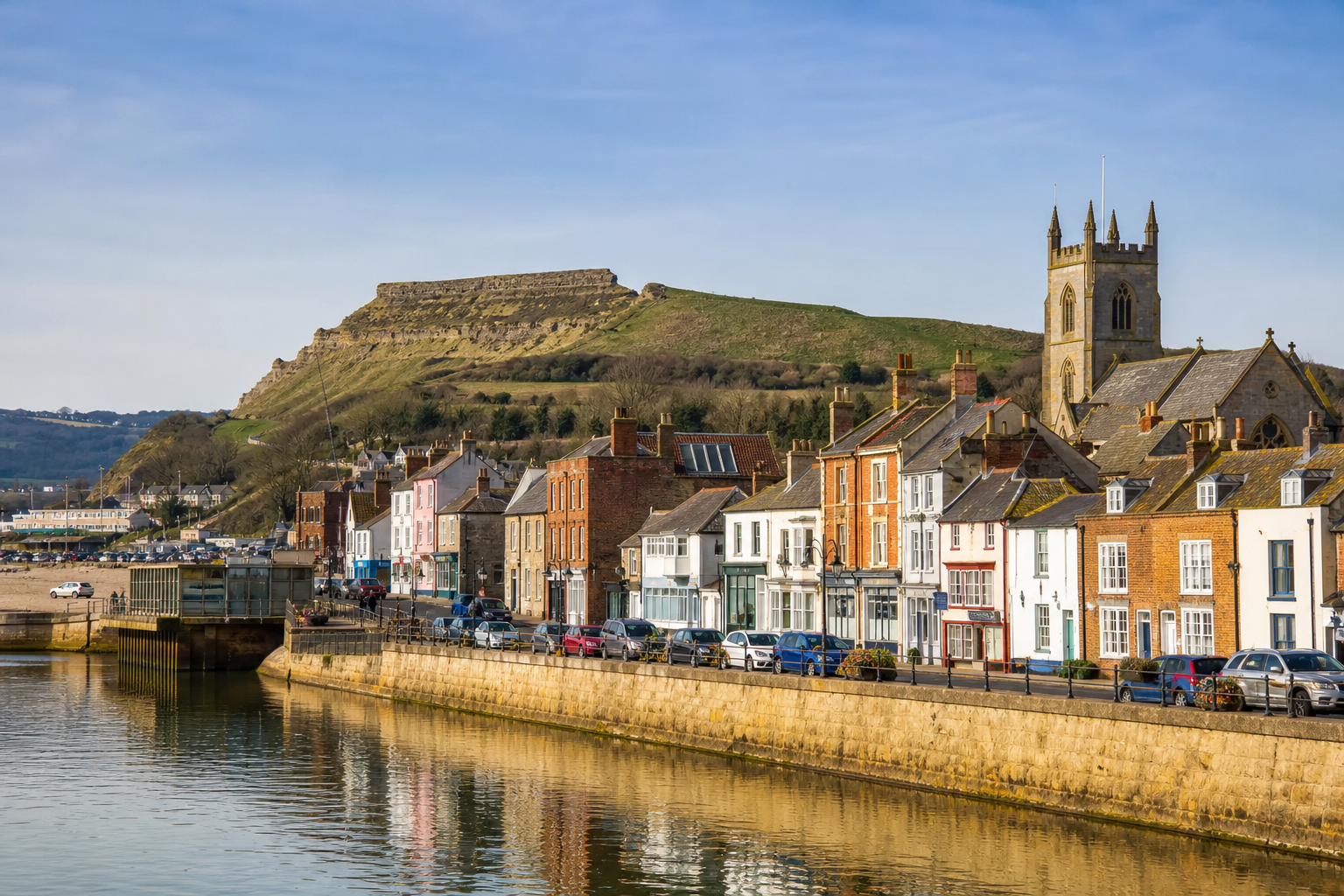 Scenic view of a coastal town with colorful buildings and a church near a grassy hill.