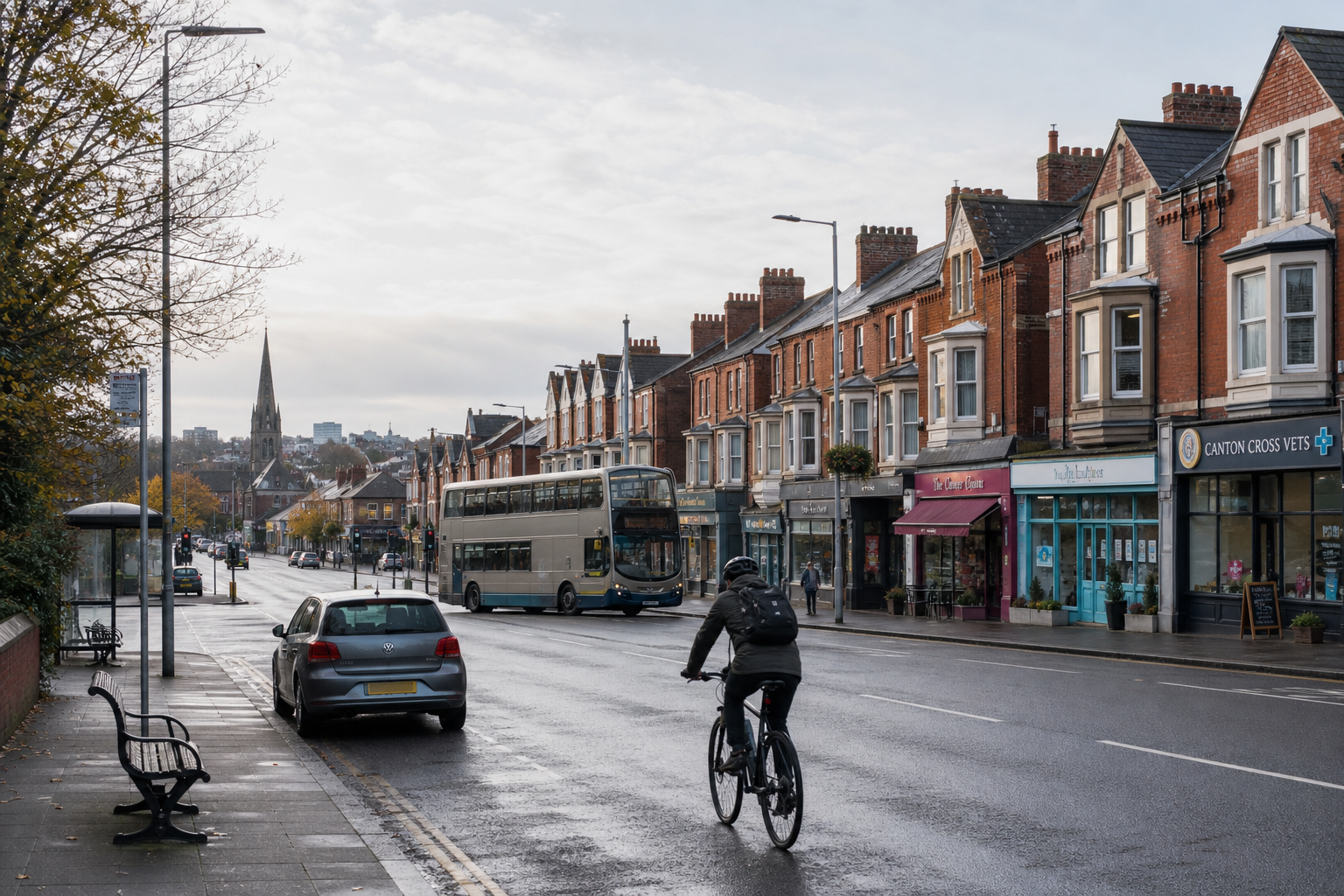 Cyclist on a city street with a double-decker bus, parked cars, and terraced shops, leading to a distant church spire.