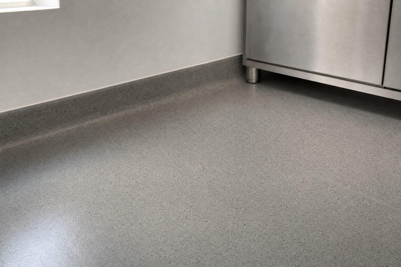 A clean, modern kitchen corner with grey speckled flooring and stainless steel cabinets.