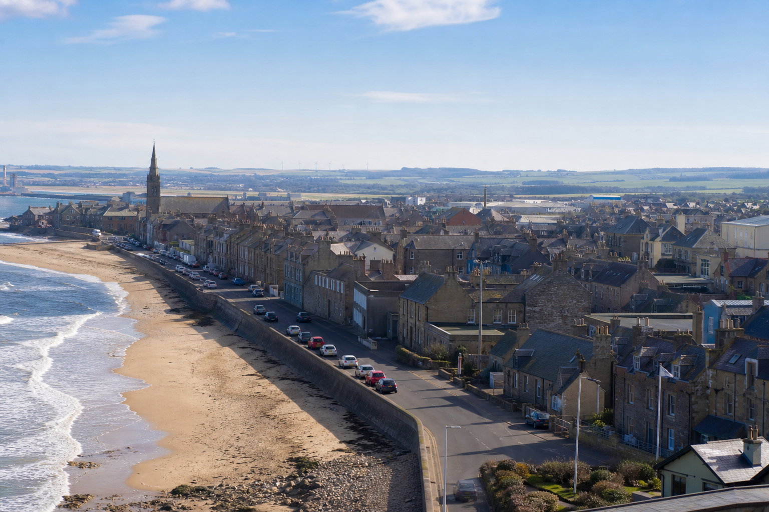 Coastal townscape with stone buildings, a church spire, and a sandy beach along a winding shoreline.