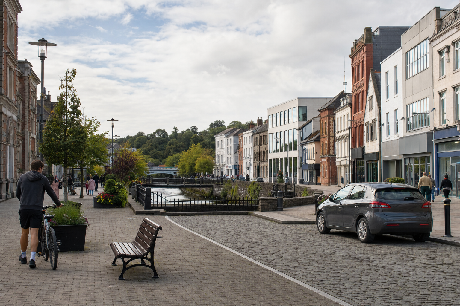 Cyclist walking beside a river in a charming town with historic and modern buildings under a partly cloudy sky.