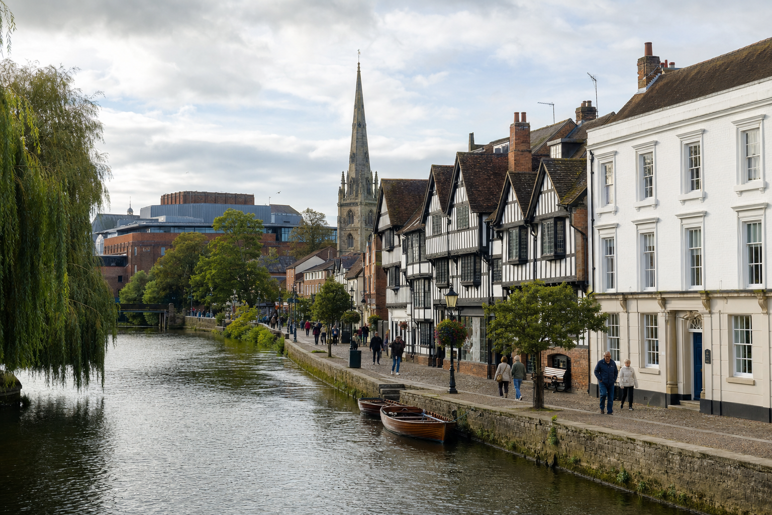 Riverfront street in Stratford-upon-Avon with timber-framed buildings and people walking along the path.
