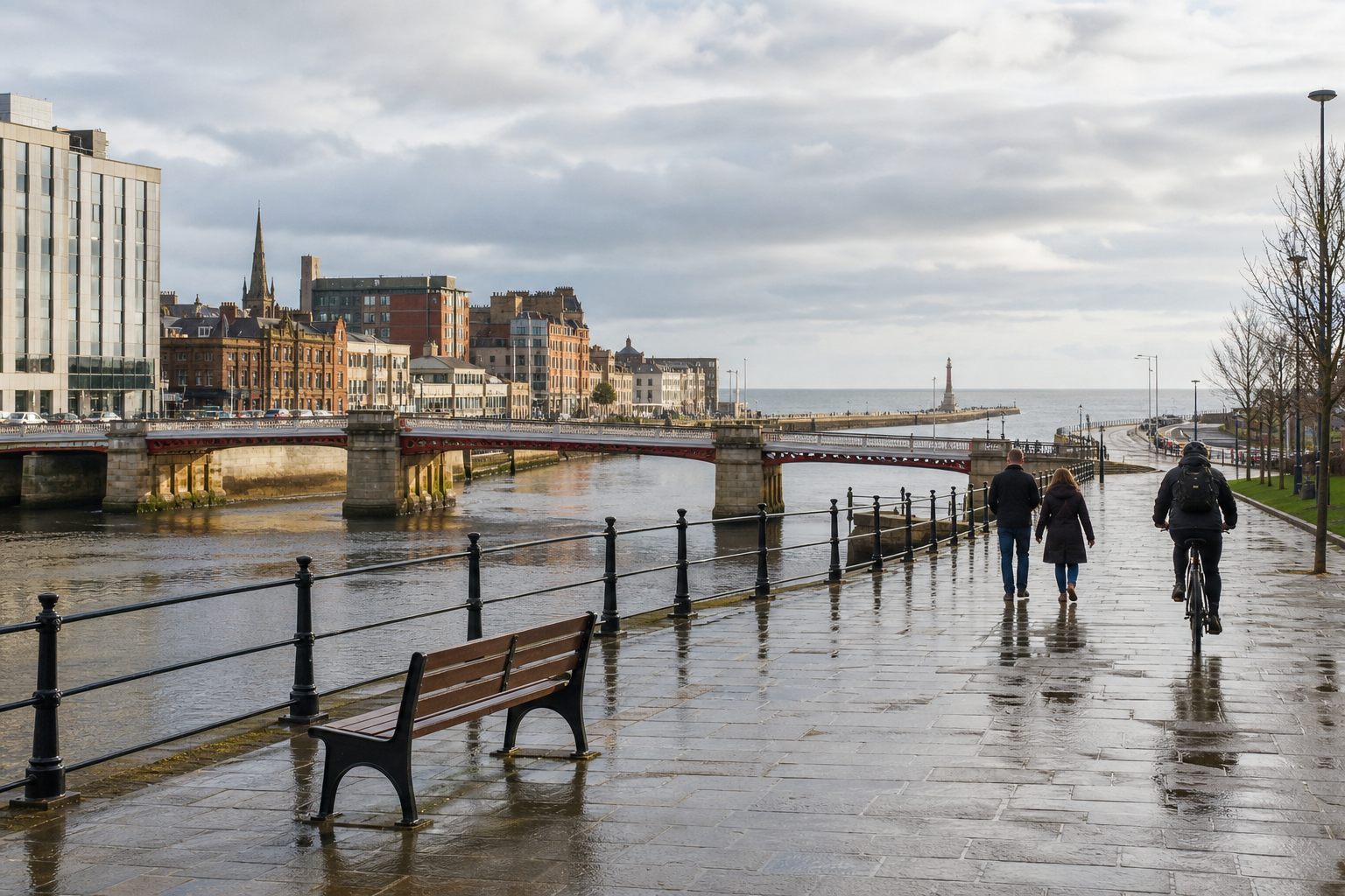 People walking and cycling along a wet riverside walkway with a bridge and cityscape in the background.