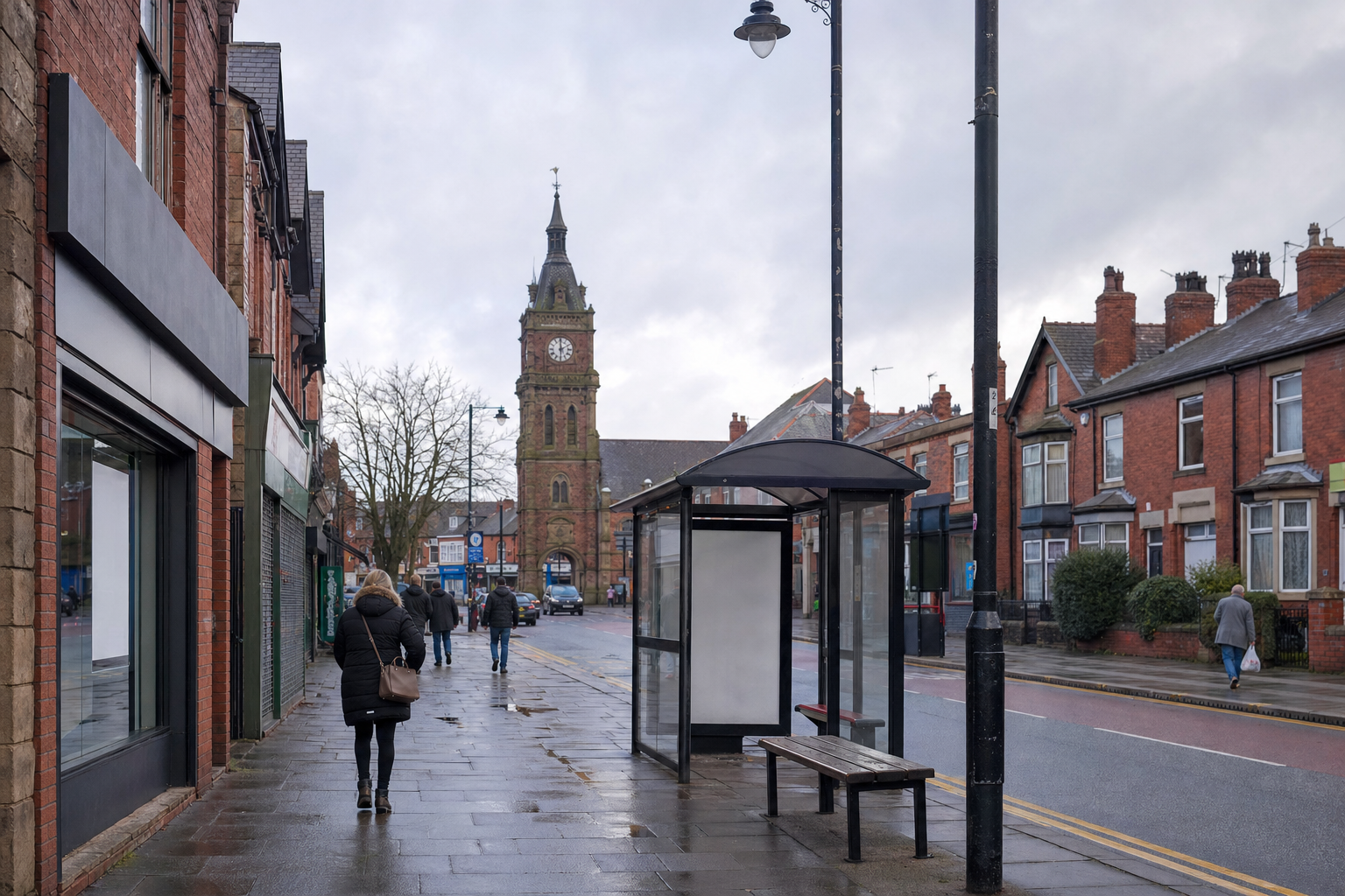 Street scene with people walking along a pavement lined with red brick buildings and a clock tower in the distance.